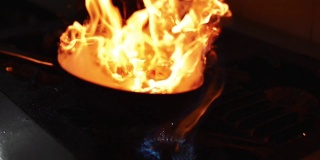 厨师拿着平底锅或炒锅搅拌或在餐厅厨房用火或火焰烹饪。