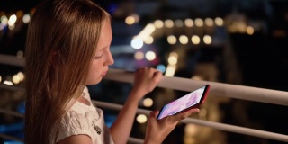 少女在黑暗的阳台上用智能手机在社交网络上观看在线直播。少女用手机在线聊天的夜晚灯光背景在阳台上。