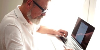 一个用笔记本电脑在家工作的成熟男人。正在工作的作家或科学家。一位老人用电脑写信，远程工作，自由职业