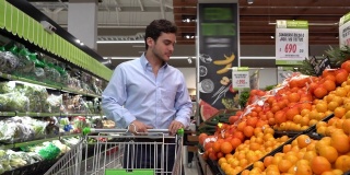拉丁美洲男子推着购物车从超市的水果摊上挑选橙子