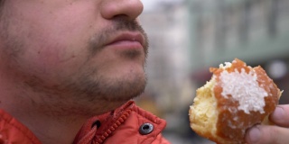 一名男子在城市街道上吃传统的波兰甜甜圈