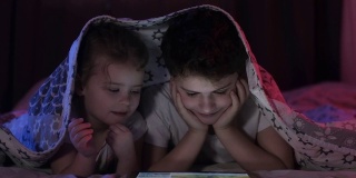弟弟和妹妹用平板电脑看视频。霓虹灯照明。