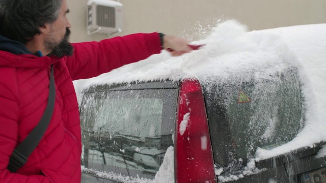 在雪地里开车。成熟的男人在第一场雪后清理汽车。活跃的老年人。