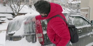 在雪地里开车。成熟的男人在第一场雪后清理汽车。活跃的老年人。