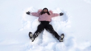 年轻快乐微笑的女孩躺在雪地里，冬天视频素材模板下载