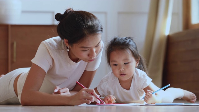 有爱心的亚洲妈妈帮助孩子的女儿用铅笔画画