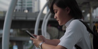 悲伤的亚洲女人站在城市街道上用智能手机。负面情绪