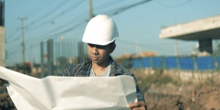 慢动作亚洲工程师男子戴安全帽和检查蓝图在施工现场，工程师建筑师施工现场规划概念