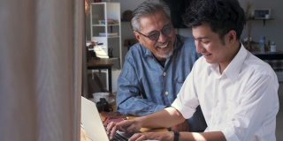 亚洲老父亲和他成年的儿子坐在家里使用笔记本电脑