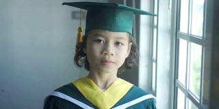 亚洲小学女生戴着毕业帽，穿着毕业服，站在学校里微笑着