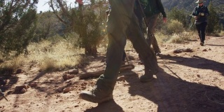 慢动作拍摄的一小群人的脚和远足杆，因为他们一起徒步在沙漠地形在一个阳光明媚的日子