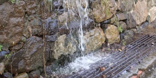 雨水落在粗糙的石头墙附近的下水道炉排上。水滴散落在两侧