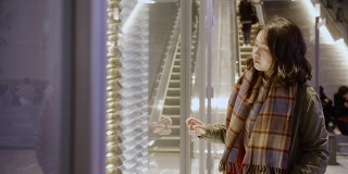 在一个寒冷的夜晚，一个亚洲女孩站在城市商店的橱窗外，她穿着暖和的衣服。