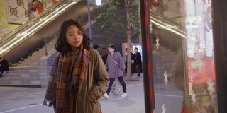 亚洲女孩妇女站在商店的窗户外，在一个寒冷的夜晚在城市里寻找圣诞礼物，她穿着暖和的衣服。
