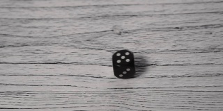 黑色骰子在一张白色纹理的旧木桌上滚动