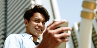 一个快乐的年轻人在城市使用手机。轨道。缓慢的运动。现代建筑背景