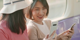 两个年轻的亚洲女人在火车上一边聊天一边用手机，慢镜头