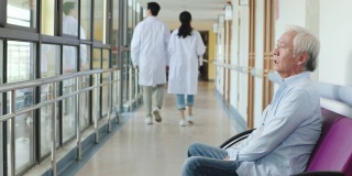 年长的亚洲人坐在医院走廊上，看起来悲伤和崩溃