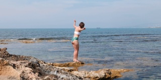 年轻的白人褐发女人在她的腿上的脂肪团沿着岩石海滩的海岸走