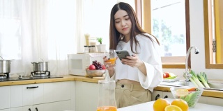 快乐的亚洲女人在厨房喝橙汁，健康的饮食和健康的概念。