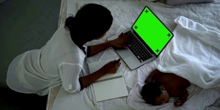 4K黑人女性使用绿色屏幕的笔记本电脑照看新生儿