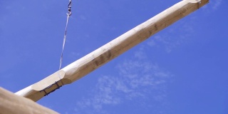 起重机在蓝天的背景下吊起横梁。夹。建筑工地的起重机将经过重处理的木材运送到建筑工地