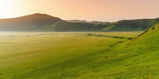 在意大利翁布里亚的卡斯泰卢西奥，阳光明媚，田园诗般的绿色景观上，雾逐渐消散