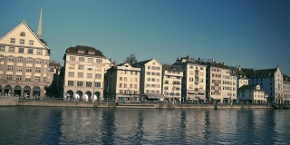 在一个阳光明媚、天空湛蓝的日子里，瑞士苏黎世州的利马特河上有著名的弗劳姆蒙斯特教堂，历史悠久的苏黎世市中心美景尽收眼底