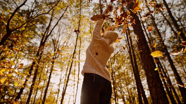 MS超级慢动作旺盛的年轻女子扔金秋的树叶在森林上空