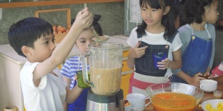 一群亚洲孩子在学校的厨房里准备水果奶昔，学习和教育的概念
