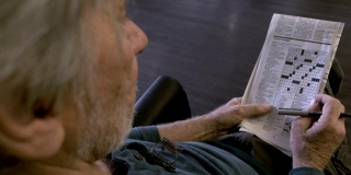 一位老人坐在椅子上玩着OTS报纸上的填字游戏