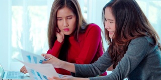 肖像亚洲美丽的女孩或妇女的手使用电脑在工作场所的业务。两名20-30岁的亚洲女孩正在核对桌上文件中的数据和报告。