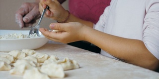 祖母和孙女正在家里的厨房里用奶酪包饺子