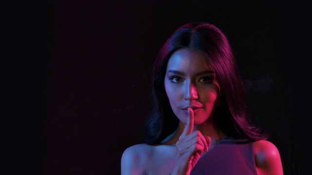 肖像拍摄的年轻调情可爱的亚洲女人调皮摆姿势的相机在粉红和蓝色霓虹灯在慢动作。