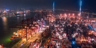码头商埠和工作吊车桥在晚上装卸集装箱到集装箱船，用于商业物流，进出口，航运或运输
