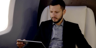 这是一幅年轻的首席银行家董事、男性政治家在私人飞机上用平板电脑阅读新闻的肖像