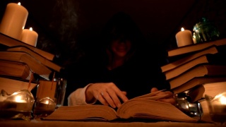 中近距离的女孩魔术师在一个黑暗的房间在烛光下寻找一个咒语翻书。低调。神秘的小景深视频素材模板下载