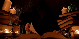 中近距离的女孩魔术师在一个黑暗的房间在烛光下寻找一个咒语翻书。低调。神秘的小景深