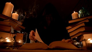 中近距离的女孩魔术师在一个黑暗的房间在烛光下寻找一个咒语翻书。低调。神秘的小景深视频素材模板下载