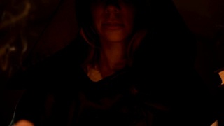 一个女孩微笑的脸在黑暗的房间里的蜡烛的黑色魔法兜帽的特写。万圣节假期和化妆舞会。神秘的。小景深视频素材模板下载