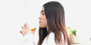 侧视图:年轻的泰国妇女喝橙汁作为早餐在早上的周末