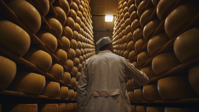 一个奶酪制作者正在控制帕尔玛干酪的调味料，这是一个古老的意大利传统成熟了好几个月