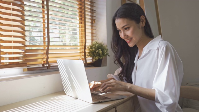 一个亚洲女人一边用笔记本电脑工作一边喝咖啡