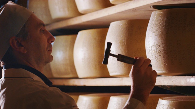 一个奶酪制作者正在控制帕尔玛干酪的调味料，这是一个古老的意大利传统成熟了好几个月