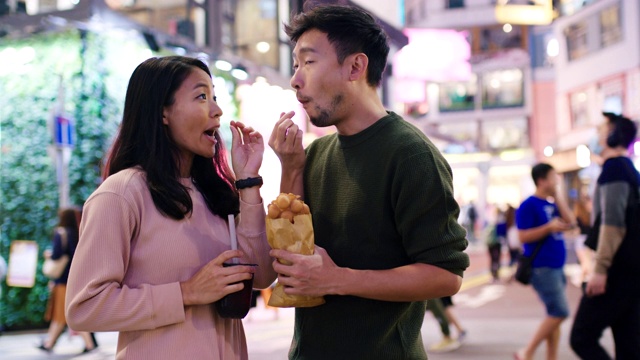SLO MO手持中景拍摄一对年轻夫妇在香港吃传统街头小吃