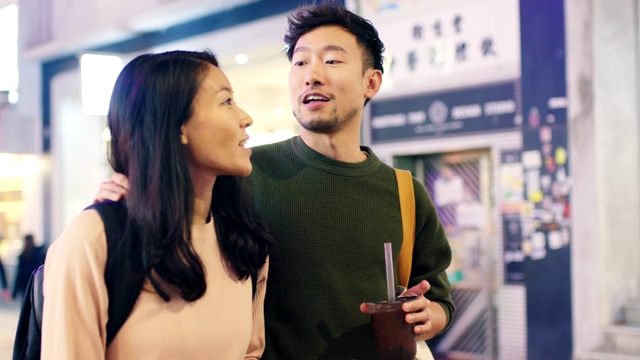 SLO MO手持式中景:一对年轻夫妇在夜晚穿过香港