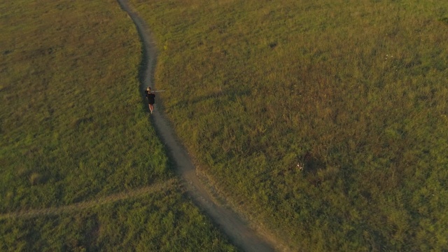 无人机拍摄的女孩肩上扛着铲子在海边的草地上行走