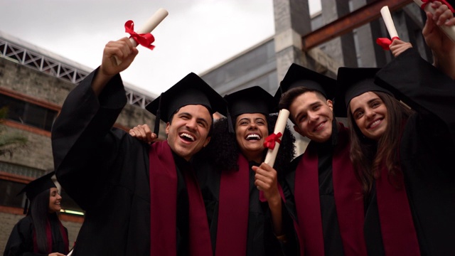 各种各样的朋友拥抱庆祝他们获得了他们的大学文凭微笑