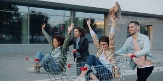 一群朋友学生在城市里骑着购物手推车开心地笑