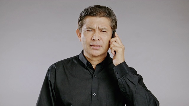 高级男子说话，手机，严肃，孤立在灰色背景。穿着黑衬衫的亚洲人。